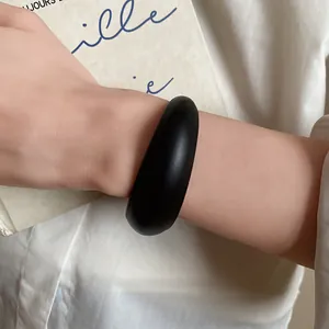 Close-up of a minimalist matte black acrylic chunky bangle worn on a model's wrist.