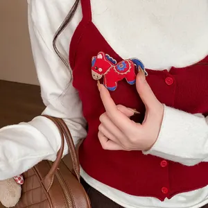 Detailed view of an embroidered red horse brooch pinned on a stylish red knit vest