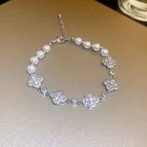 Close-up of elegant pearl bracelet with zircon-studded four-leaf clover charms.