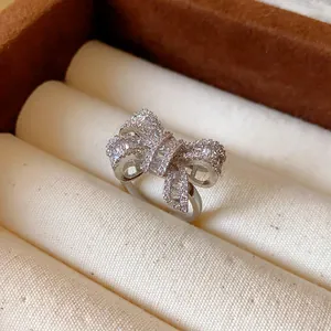Macro view of an elegant silver bow-shaped open ring with pavé-set zircons in a box.
