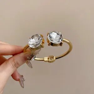 Close-up view of two large oval-shaped clear crystals on a gold-finished open bangle