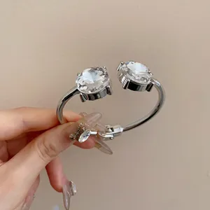 Close-up detail of a silver-toned open bangle featuring two large round sparkling crystals.