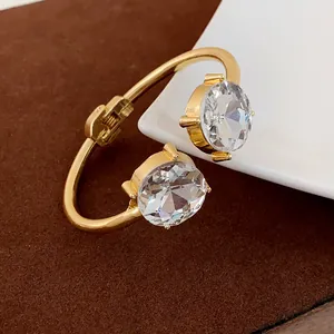 Detail of a gold-plated open cuff bracelet featuring two large round-cut clear crystals