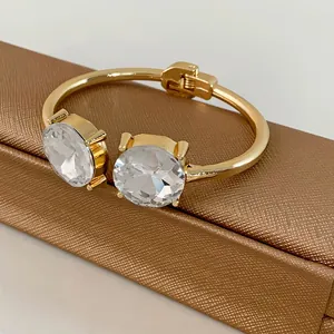 Close-up view of elegant gold open bangle featuring two large round faceted clear crystals