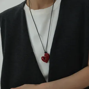 Primo piano di un ciondolo a cuore rosso irregolare su una collana regolabile nera.