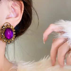 Close-up of elegant vintage purple oval ear clip with ornate gold floral and pearl border