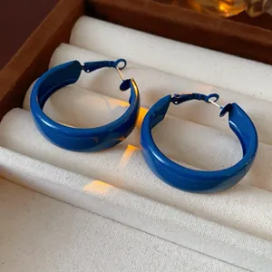 Detailed macro shot of vibrant blue geometric C-shape hoop earrings on a velvet tray