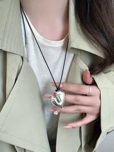 Primo piano di un ciondolo a cuore in argento su cordino nero indossato con un cappotto beige.