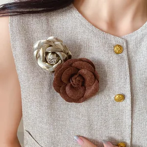 Close-up detail of elegant brown flocked and silver metallic leather camellia brooches on tweed