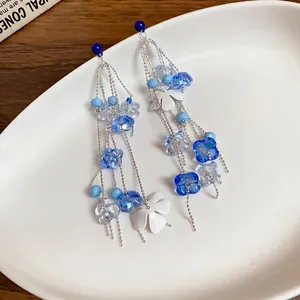 Pendientes de borla de cuentas de vidrio azul sobre fondo de plato de cerámica blanca arte