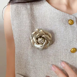 Detailed view of an elegant golden leather rose brooch pinned to a stylish beige tweed vest.