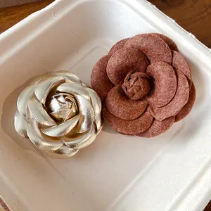 Close-up detail of elegant gold leather and reddish-brown flocked camellia flower brooches