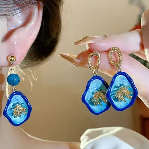 Exquisite close-up detail of blue vintage floral drop earrings shown on ear and hand
