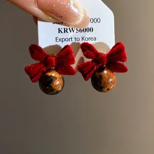 Dettaglio dei orecchini a fiocco rosso floccato con perle in resina ambrata.