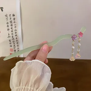 Close-up detail of a light green wavy hair stick with pink flower tassels and pearls.