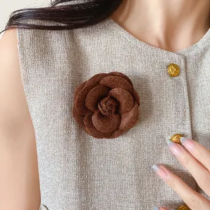 Close-up of elegant brown flocked camellia flower brooch on textured beige top