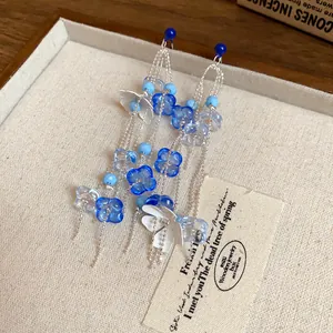 Detalle de elegantes pendientes de borla de flores con cuentas de vidrio azul en bandeja de lino