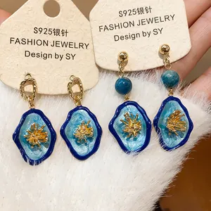Close-up of blue enamel flower earrings with S925 silver needles on a display card.