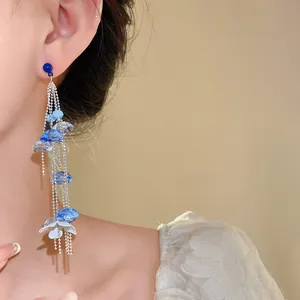 Detalle de pendientes de borla larga con cuentas de vidrio azul y pétalos blancos.