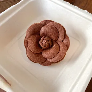 Detail view of an elegant brown flocked leather camellia flower brooch for women