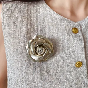 Close-up detail of an elegant gold leather camellia flower brooch on beige textured fabric