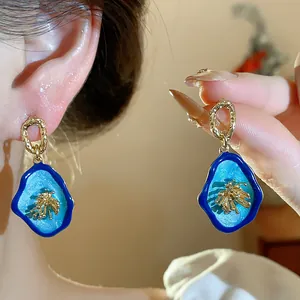Detail of vintage blue enamel earrings with golden flower motif on an ear.