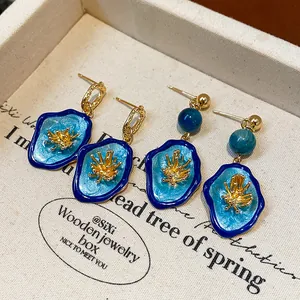 Detail shot of blue enamel flower earrings with gold accents in a jewelry tray