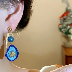 Elegant blue enamel flower drop earrings with silver pins shown on a model's ear.