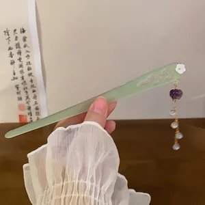 Close-up detail of a pale green Chinese hair stick featuring a heart tassel and gold chain