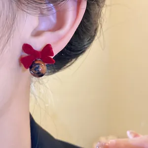 Primo piano di un orecchino a fiocco rosso floccato con perla leopardata su un orecchio.