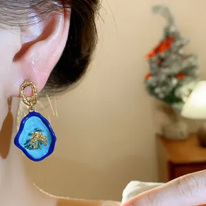 Detailed close-up of vintage blue enamel earrings with intricate gold flower design on ear