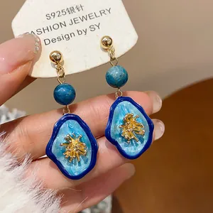 Detail of S925 silver needle earrings with blue resin and gold flower clusters
