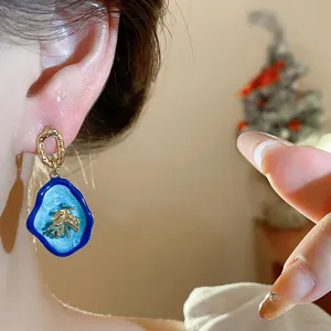 Close-up of vintage blue enamel earrings with gold flower detail on a silver needle