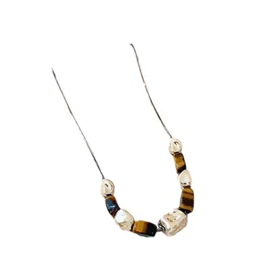 Irregular wrinkled silver bead necklace with tiger eye stones on white background.