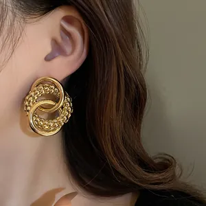 Macro detail of chunky gold knotted hoop earrings with textured finish on model.