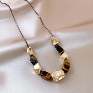 Close-up detail of irregular crumpled gold beads and synthetic tiger-eye stones on necklace