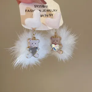 Close-up of fluffy white pom-pom earrings with cute bear and crystal heart charms