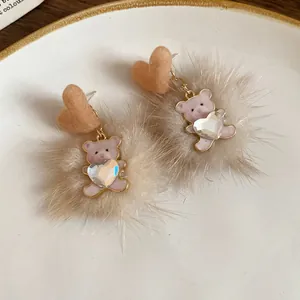 Close-up detail of teddy bear earrings with soft fur balls and heart-shaped crystals.