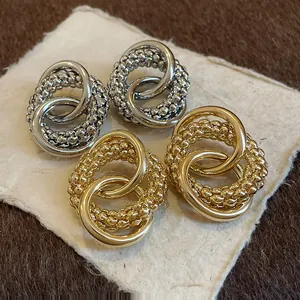 Detailed macro view of gold and silver circular knotted earrings shown on textured paper