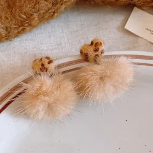 Close-up detail of leopard print heart and tan faux fur pom pom autumn winter earrings