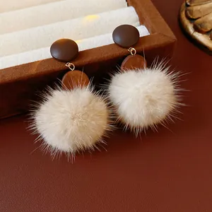Close-up view of elegant beige fluffy pom-pom earrings with dark brown wooden studs
