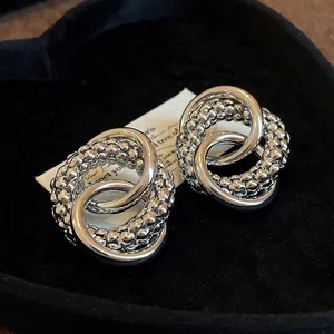 Macro view of silver knotted stud earrings featuring smooth and textured intertwined rings