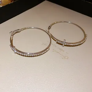 Close-up of silver-tone hoop earrings with rhinestone cross charm detail.