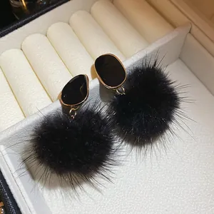 Close-up of black fur ball earrings with gold-framed studs in a jewelry box