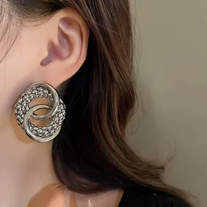 Close-up of silver knotted circular earrings with textured and smooth interlocked rings.