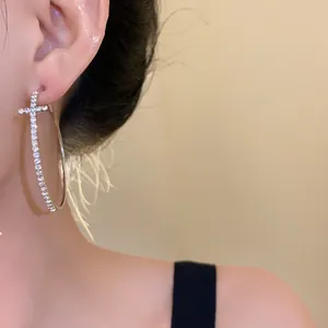 Close-up detail of a elegant silver cross hoop earring with sparkling crystals on a model