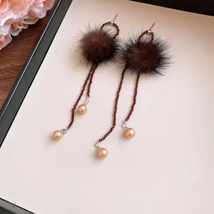 Close-up of elegant brown fur ball earrings with beaded tassels and champagne pearls.