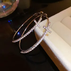 Close-up detail of silver needle hoop earrings with pavé diamond cross design