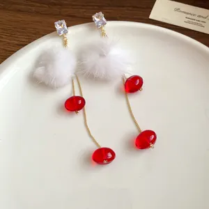 Close-up of elegant long dangle earrings with white fluffy pom-poms and red glass beads