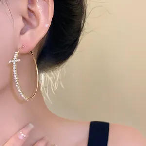 Close-up view of gold hoop earrings with a rhinestone cross on an Asian model's ear.